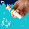 1 miniature mermaid toy being held by a child's hand against an illustrated background. pale skinned with low black bun.