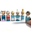 7 Cinderella wooden toy dolls standing in a row. Prince being held by child’s hand. 1 evil stepmother, 2 evil stepsisters, 1 cinderella in rags, 1 fairy godmother, 1 cinderella in fancy dress, 1 prince.
