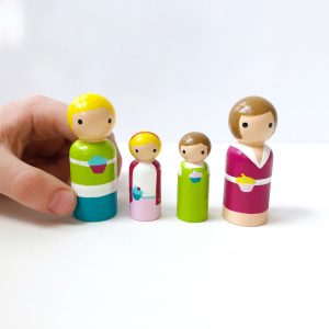 3 small toy family figures standing in a line. One being held by a child’s hand. 1 mother, 1 boy, 1 girl, and 1 dad