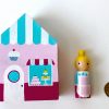 1 wooden bakery block toy and one female bakery worker standing next to a Quarter for size comparison.