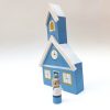 sideview of blue mini wooden schoolhouse toy with pale skinned, gray haired teacher standing next to it.