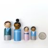 4 miniature wooden toys for kids standing in a row next to a quarter for size reference. 1 African American woman, one pale skinned man, 1 medium toned boy, 1 pale skinned girl all dressed in 19th Century Aristocrat attire.