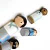 close up of 4 Farmhouse style Peg dolls laying down, coming out of a bag. 1 medium skinned man with black hair, 1 pale skinned woman with black hair, 1 pale skinned boy with brown hair, 1 dark skinned girl with black hair.